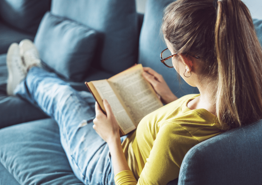 femme qui lit allongée dans son canapé comme moyen de décompression
